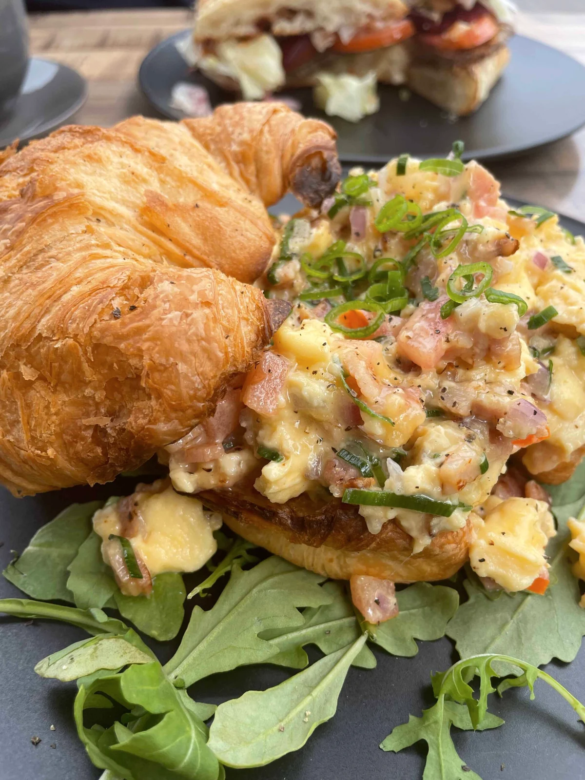 Golden croissant with loaded scrambled eggs, bacon and fresh greens at Ellen and Rod