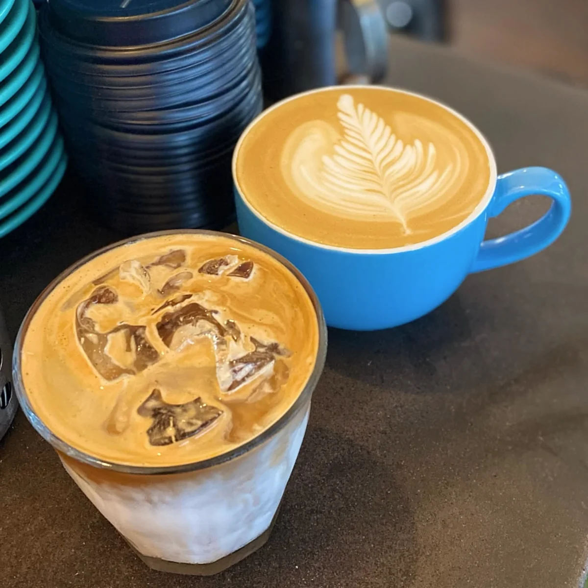 A fresh hot coffee in a blue cup beside an iced coffee at Ellen and Rod